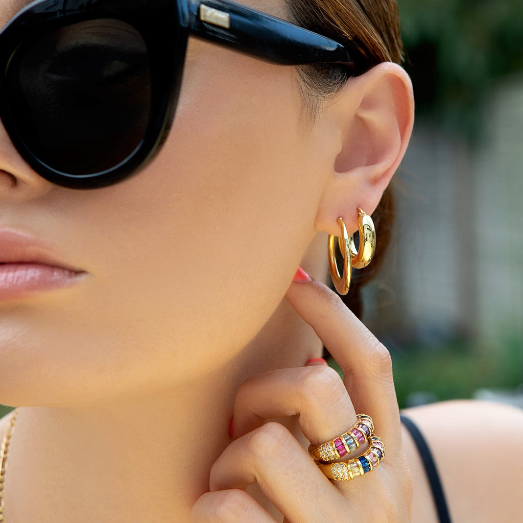 Model wearing gold hoop earrings and Multi-coloured baguette crystal and gold rings