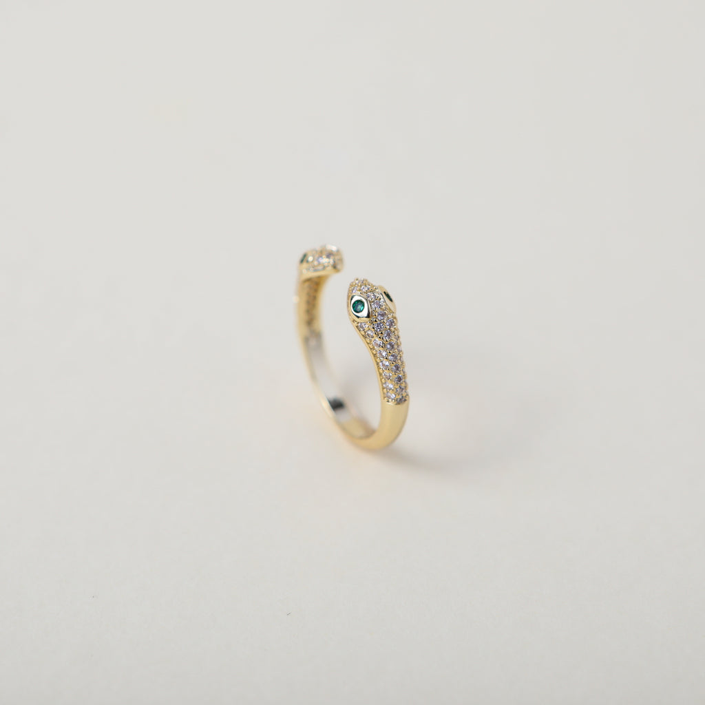 Gold and crystal accented open claw ring featuring two snake heads with green crystal eyes green eyes